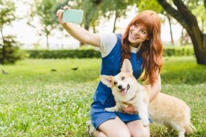 Caucasian red-haired woman young teenager girl taking selfie photo together with her welsh corgi dog