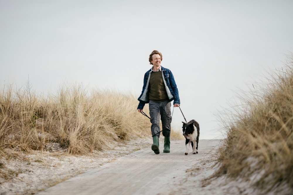 Middle aged caucasian man walking his border collie dog on a winter beach